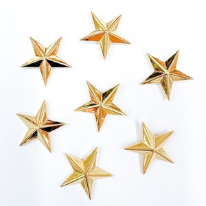 May include: Seven gold-colored five-pointed stars on a white background. The stars are arranged in a random pattern.