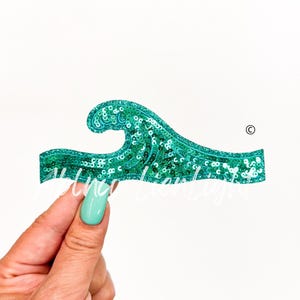 May include: A teal blue wave-shaped sequin patch. The patch is made of sequins and has a shiny finish.