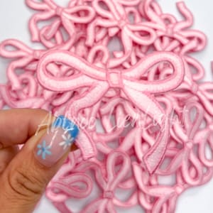 May include: A pile of pink felt fabric bows. The bows are all the same size and shape, and they are arranged in a random pattern.