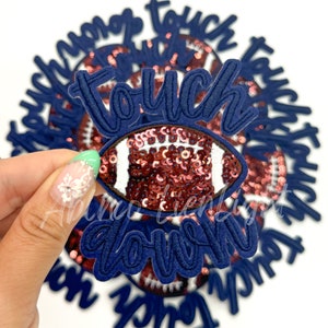 May include: A close-up of a blue and white iron-on patch with the words "touch down" and a sequined football design.