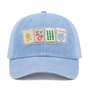 K&ouml;nnte beinhalten: Hellblaue Jeans-Baseballkappe mit Mesh-R&uuml;ckseite. Auf der Vorderseite befinden sich vier gestickte Aufn&auml;her mit chinesischen Schriftzeichen, Blumen, Bambus und dem Wort "JOKER". Die Aufn&auml;her sind mit silbernem Glitzer umrandet.