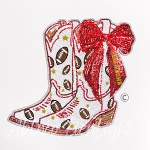 May include: White cowboy boot design with footballs and gold stars, adorned with a large red sequined bow. The boot features a brown heel and is embellished with sequins. A decorative item for football fans.