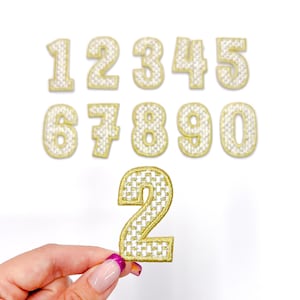 May include: Ten gold iron-on patches with white checkered designs, featuring the numbers 1 through 10. The number 2 is being held by a hand.