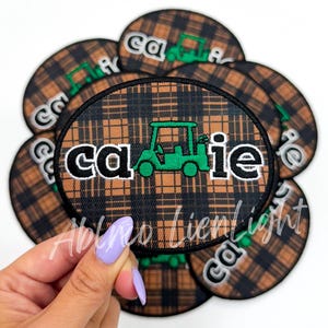 May include: A set of brown and black plaid iron-on patches with the word "cadie" and a green golf cart design.