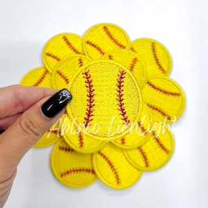 May include: A close-up of a pile of yellow and red softball patches. The patches are round and have a stitched design.