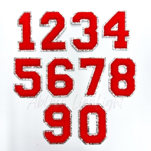 May include: Ten red felt iron-on numbers with a silver glitter outline. The numbers are 1, 2, 3, 4, 5, 6, 7, 8, 9, and 0.
