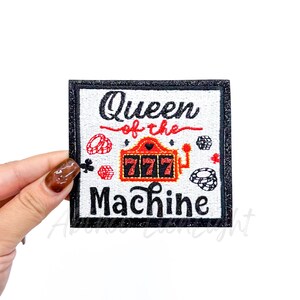 May include: Square patch with a black glitter border and the words "Queen of the Machine" in black and red. The patch features a slot machine, dice, and casino chips.