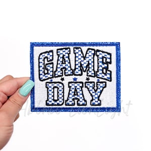 May include: Blue and white embroidered patch with the text "GAME DAY" in a checkered pattern. The patch has a blue border.
