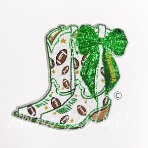 May include: A decorative patch shaped like a cowboy boot, covered in white, green, and brown sequins. The boot features a pattern of brown footballs and gold stars, accented with a large, bright green sequined bow and the word TOUCHDOWN.