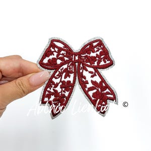 May include: A red embroidered bow with a silver glitter outline. The bow has a floral design and is perfect for adding a touch of elegance to any project.
