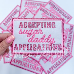 May include: Pink and white iron-on patch with glitter. The patch says "Accepting Sugar Daddy Applications".