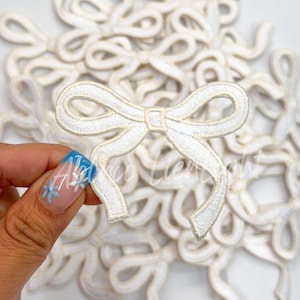May include: A pile of white embroidered fabric bows. The bows are about 2 inches wide and have a satin finish.