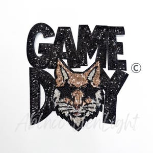 May include: Black sequined "GAME DAY" text with a stylized fox head in the center. The fox features gold and white sequin details. The design is set against a white background, creating a bold, eye-catching graphic.