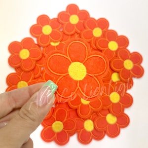 May include: A pile of 15 orange felt flower patches with yellow centers. The flowers are approximately 2 inches in diameter.