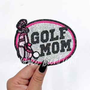 May include: A silver and pink glitter iron-on patch with a golf bag and golf ball, and the text "GOLF MOM" in black.