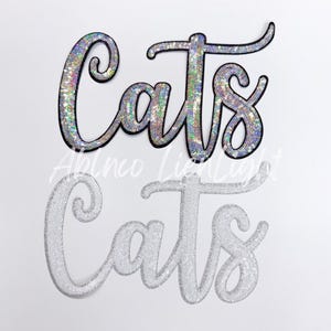 May include: Two iron-on patches with the word "Cats" in a cursive font. The top patch is silver with iridescent sequins and a black outline. The bottom patch is white with silver sequins.