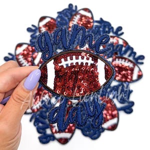 May include: A set of iron-on patches featuring a football design with red and white sequins and the words "game day" in blue.