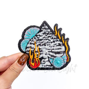 May include: A sequined ace of spades patch with a black glitter border. The card is filled with white sequins and surrounded by orange and red flames, and teal and gray accents.