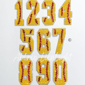 May include: Set of ten 3-inch iron-on patches featuring the numbers 1 through 10. Each number is made of yellow sequins with red stitching that resembles a baseball or softball. The patches are perfect for adding a sporty touch to clothing, bags, or other items.