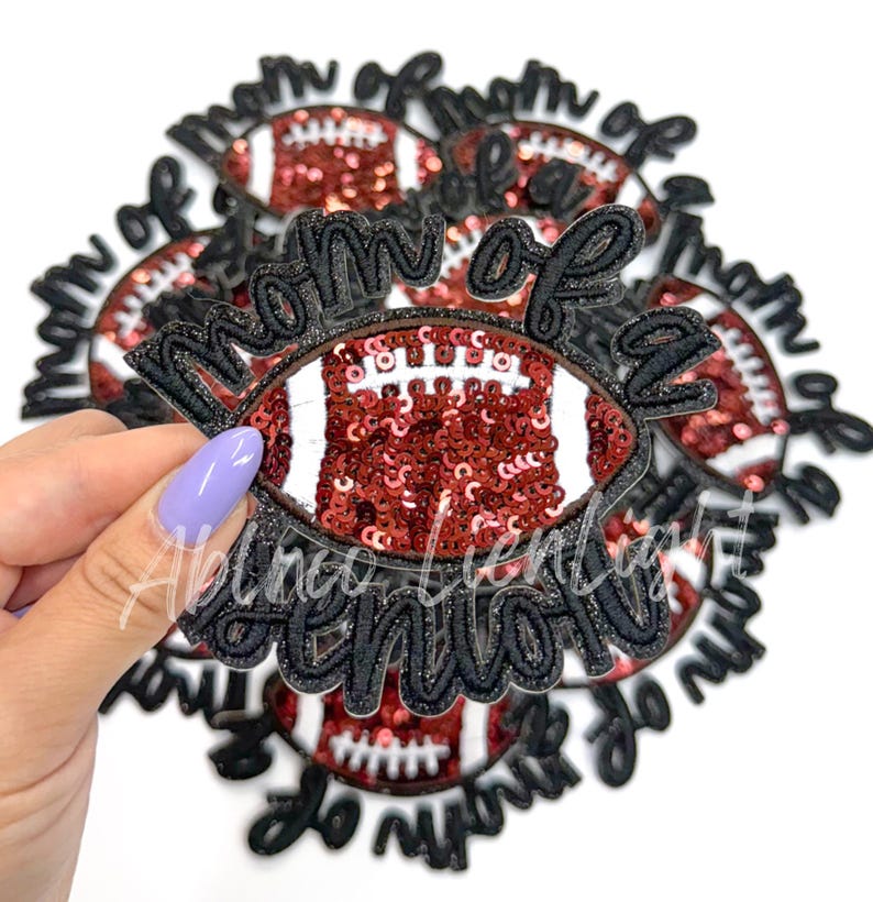 May include: A close-up of a black and red iron-on patch with the text "Mom of a Thot" and a red and white football design. The patch is surrounded by other similar patches.
