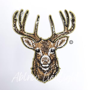 May include: A brown and gold sequined deer head applique with large antlers. The deer has a white face and black eyes.