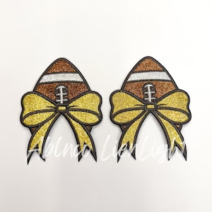 May include: Two brown and gold glitter footballs with yellow bows. The footballs have white stitching and a silver glitter design.
