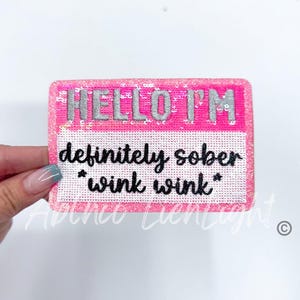 May include: Pink and white iron-on patch with silver glitter lettering that reads "HELLO I'M definitely sober *wink wink*"