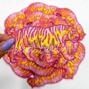 May include: A stack of pink and yellow iron-on patches featuring a tiger design. The tiger is outlined in yellow and has pink stripes.