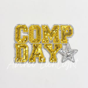 May include: Gold sequined iron-on patch with the text "COMP DAY" in a white outline and a silver star.