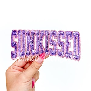 May include: Purple and pink sequined iron-on patch that says "Sunkissed".