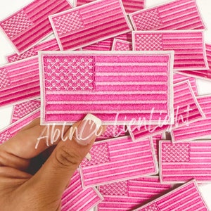 May include: A pile of pink embroidered American flag patches. The patches are all the same size and have a white outline.