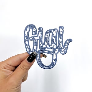 May include: A blue embroidered iron-on patch with the word "Girl" in a stylized font.