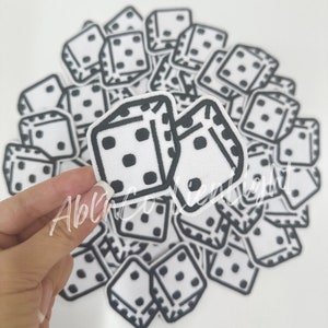 May include: A pile of white iron-on patches with black outlines of dice. Each die has black dots on the white surface.