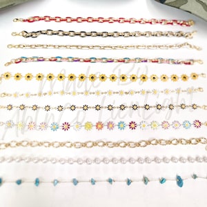 May include: A collection of 10 different chain styles, including gold chains, pearl chains, and chains with small flower charms. The chains are all laid out in a row on a white background.