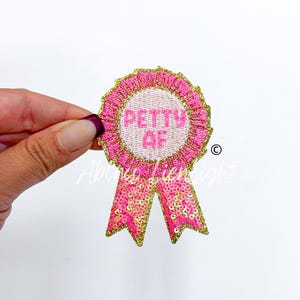 May include: Pink and gold embroidered iron-on patch with a pink ribbon and the text "PETTY AF".