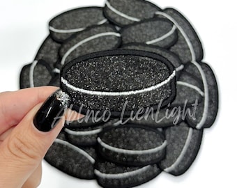 May include: A pile of black and white hockey puck patches with a white outline. The patches are made of felt and have a sparkly texture.
