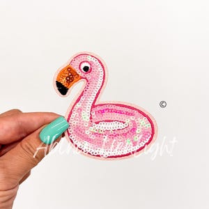 May include: Pink sequined flamingo pool float patch. The patch is made of sequins and has a pink flamingo design with a white inner tube.