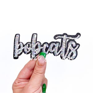 May include: A black and silver sequined iron-on patch that says "Bobcats".