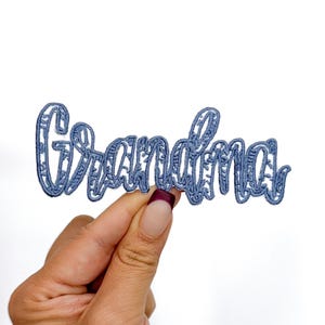 May include: A blue embroidered patch with the word "Grandma" in a decorative font.
