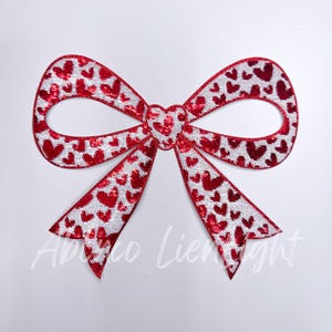May include: Red and white bow with a heart pattern. The bow is made of sequins and is perfect for adding a touch of sparkle to any project.