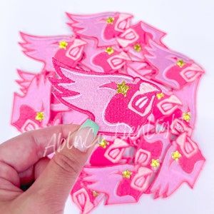 May include: A stack of pink and white iron-on patches featuring a cartoon bird with a star on its head. The patches have a glittery finish.