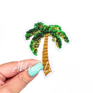 May include: A green and yellow palm tree applique with sequins. The palm tree is on a white background.