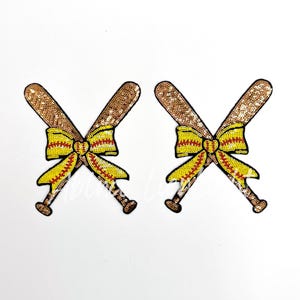 May include: Two gold sequin softball bats crossed with a yellow and red bow in the center.