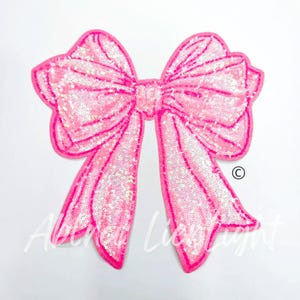 May include: A large pink sequined bow with a shiny iridescent finish. The bow is a decorative embellishment for clothing or crafts.