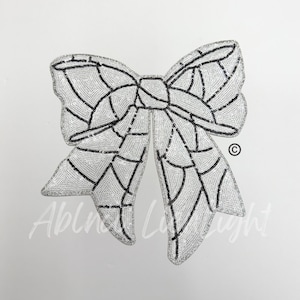 May include: A large, decorative bow with a sequined design. The bow is primarily white with black accents outlining the bow's shape. The text "Abln Light" is visible at the bottom of the bow.