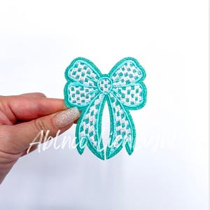 May include: A turquoise and white checkered bow with a glittery finish. The bow is a decorative patch that can be ironed onto fabric.