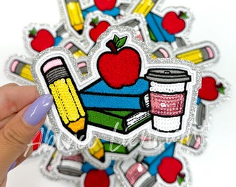 May include: A set of iron-on patches featuring a stack of books, a red apple, a pencil, and a coffee cup. The patches are decorated with sequins and have a silver glitter border.
