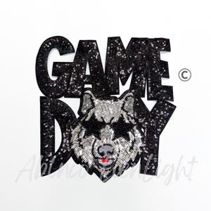 May include: Black sequined "GAME DAY" patch with a wolf design. The wolf is silver with a red tongue, and the text is in a bold, blocky font. The patch is likely for apparel or accessories.