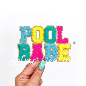 May include: A colorful felt applique with the words "POOL BABE" in gold glitter lettering. The letters are in different colors: blue, yellow, pink, and turquoise.
