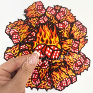 May include: A pile of red and yellow embroidered iron-on patches featuring a flaming dice design.